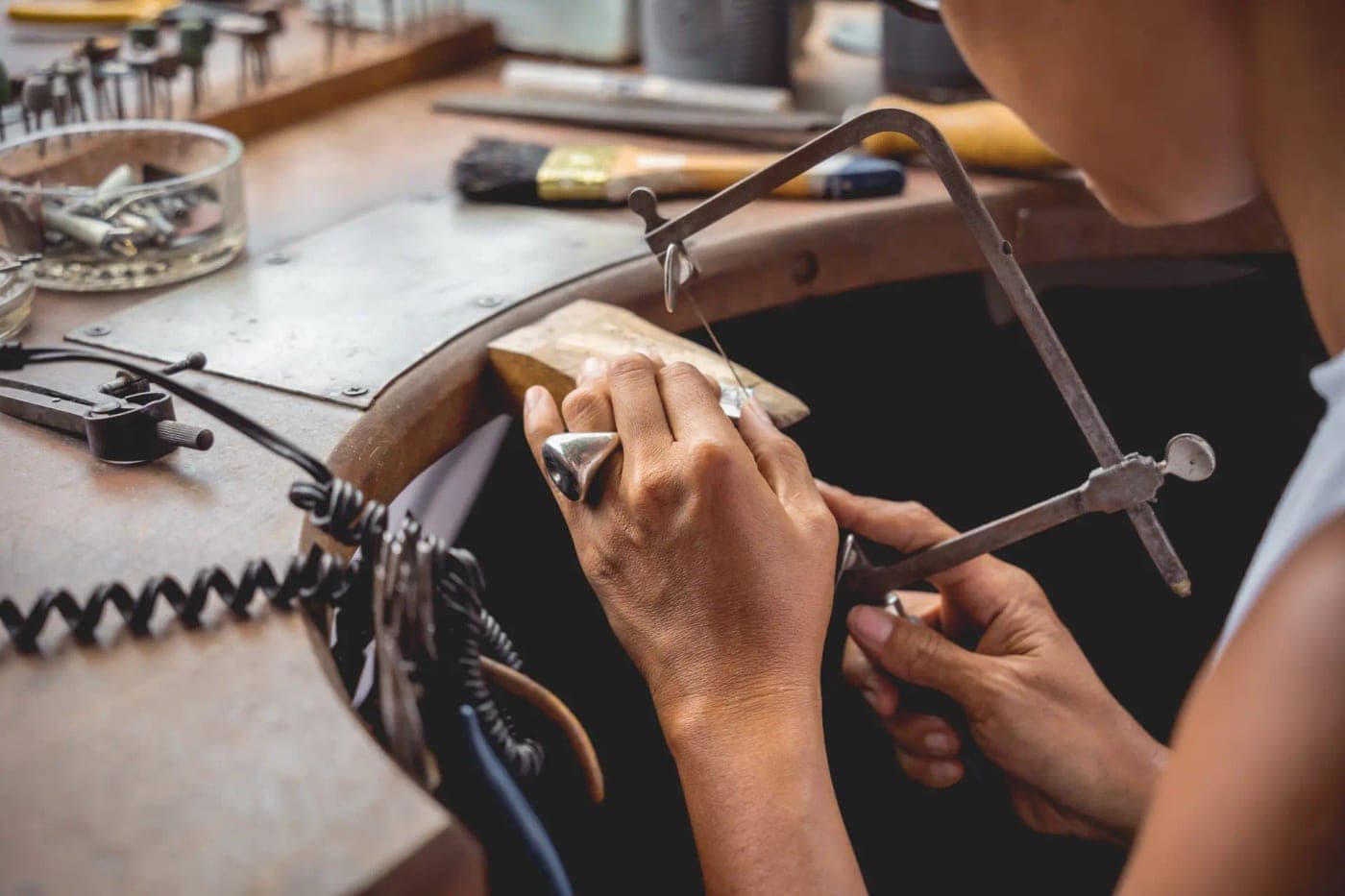 Hands cutting metal with a jeweler's saw at a workbench